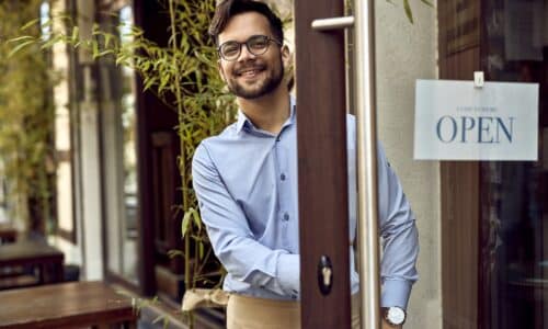 Young happy waiter standing at cafe's front door.